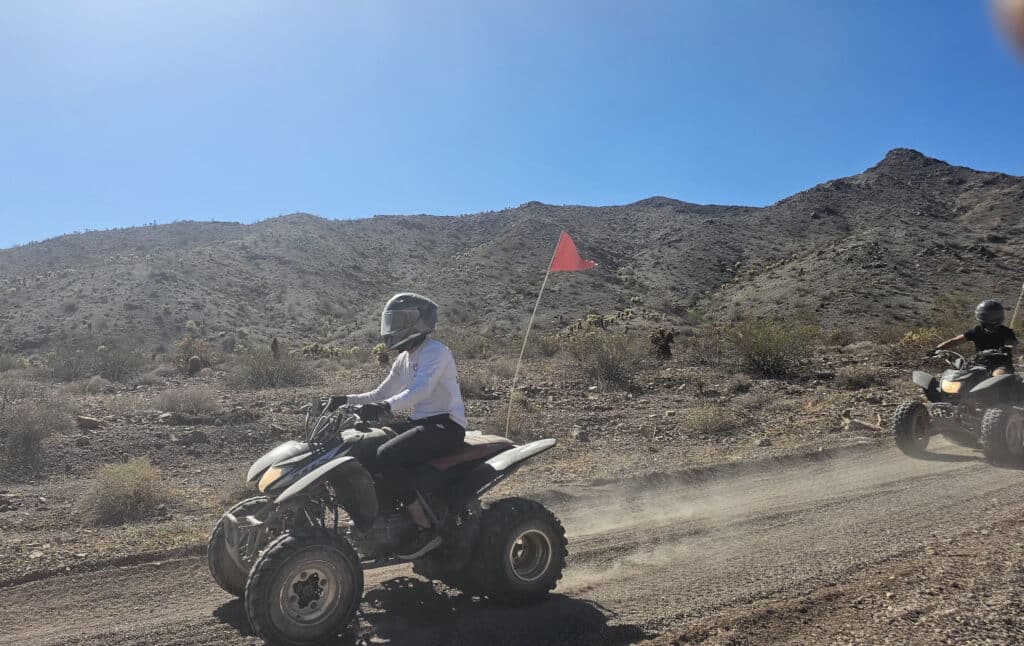 Rider in helmet on ATV with red flag explores Nevada desert trail near mountains, ideal for Las Vegas ATV tours.
