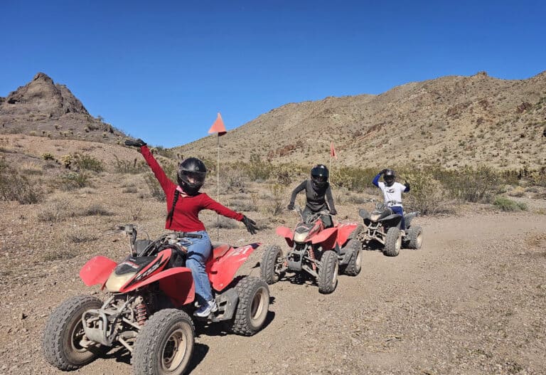 ATV riders in helmets explore a Nevada desert trail near Las Vegas, with mountains as backdrop on an exciting off-road ATV tour.