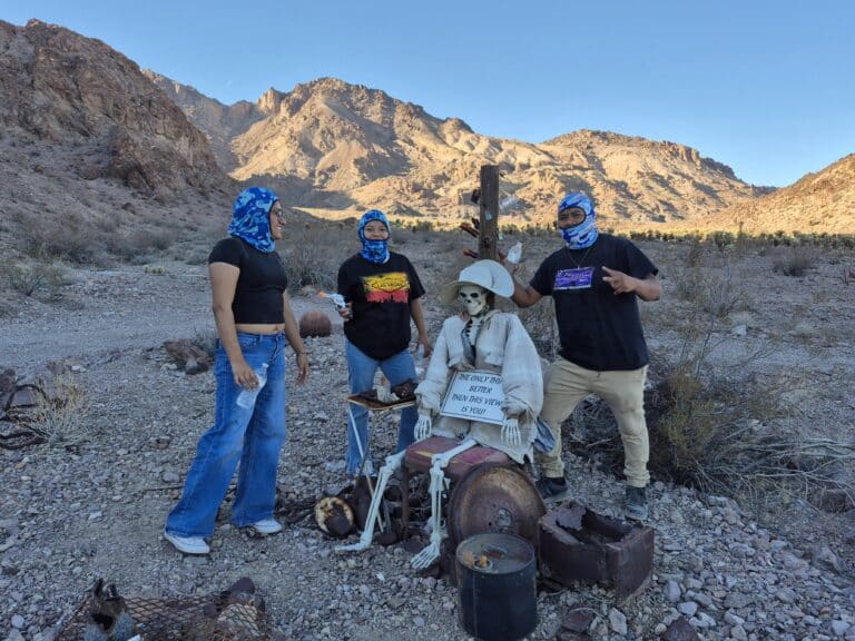Visitors in blue bandanas pose by a skeleton in a Nevada ghost town near Las Vegas during an ATV tour in the desert.