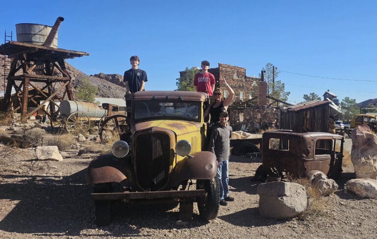 Visitors pose with a vintage car in a Nevada desert ghost town near Las Vegas, surrounded by old buildings—perfect for sightseeing.