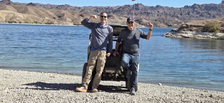 Two men pose by an ATV near the Colorado River, Nevada, with mountains and lake views—ideal for Las Vegas RZR off-road tours.