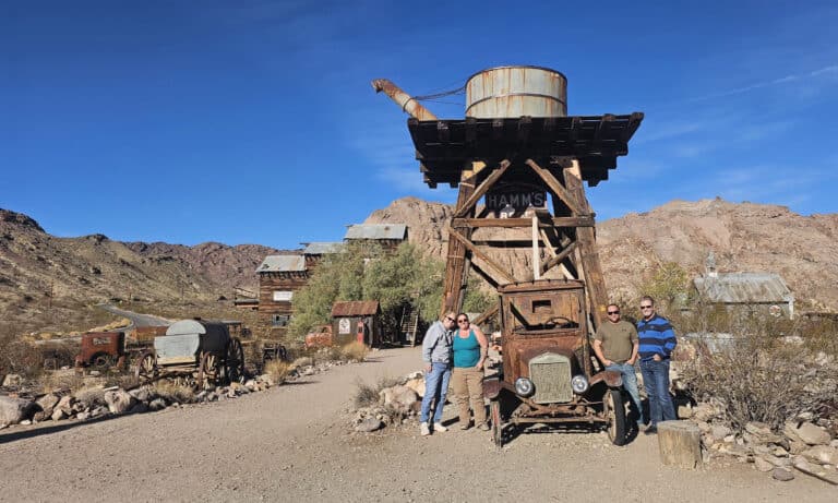 Group poses by a rusty car under a water tower in a Nevada ghost town near Las Vegas, perfect for Ghost Town sightseeing tours.
