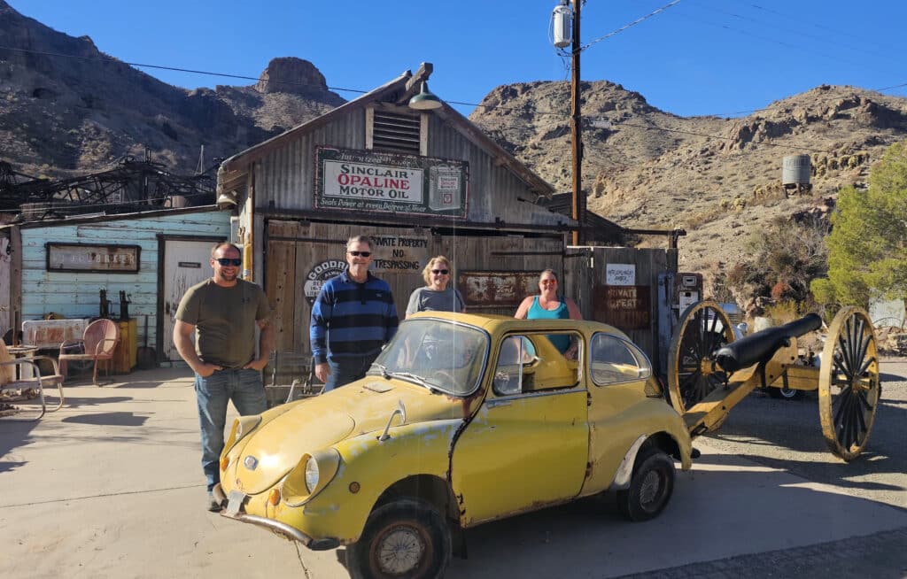 Group poses by vintage yellow car at Nevada ghost town near Colorado River, ideal for RZR tours and Las Vegas sightseeing.