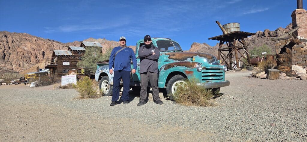 Two people by a rusty turquoise vintage truck in a Nevada ghost town near Las Vegas, ideal for ATV tours and sightseeing.
