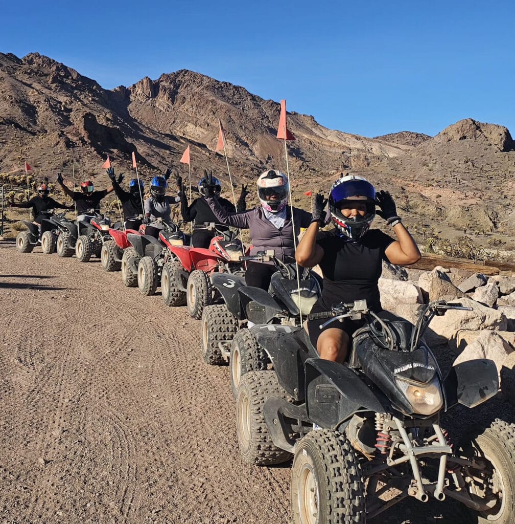 Adventurers on an ATV tour near Las Vegas ride in a line through Nevada’s rocky terrain, arms raised under a clear sky.