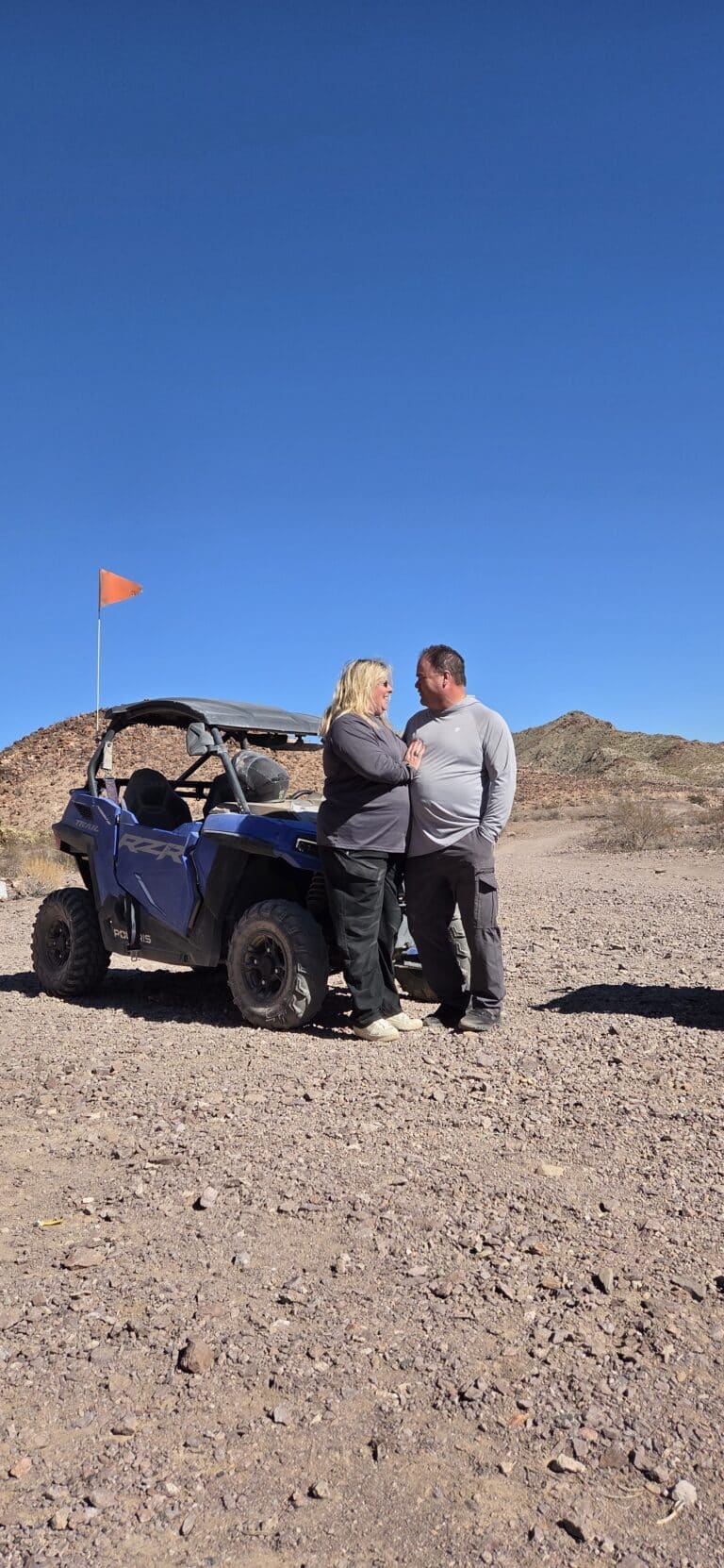 Couple poses by a blue off-road vehicle with orange flag in Nevada desert near Las Vegas, perfect for ATV tours or RZR rides.