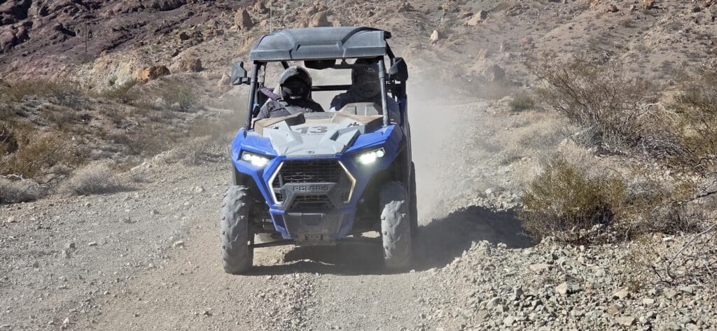 Blue off-road vehicle with two riders explores dusty Nevada desert trail near Las Vegas on an exciting RZR ATV tour.