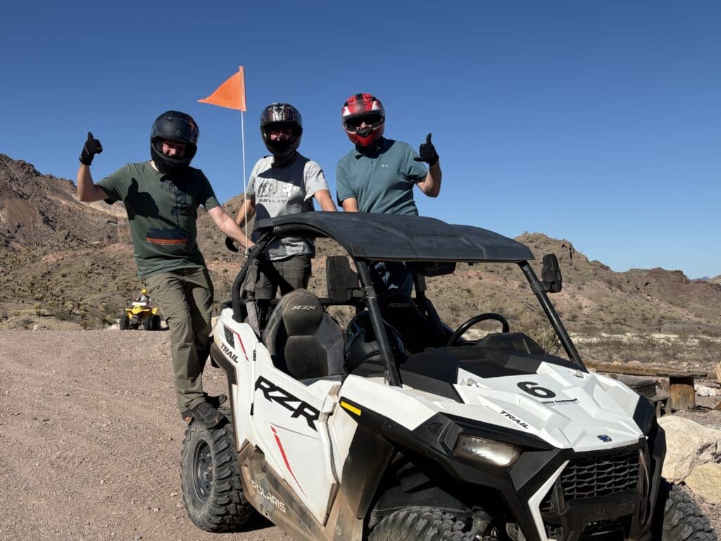 Adventurers in helmets and gloves pose by a white RZR on a rocky Nevada trail during an exciting Las Vegas ATV tour.