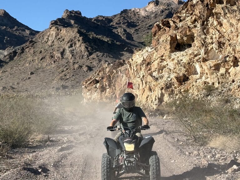 Experience an ATV tour near Las Vegas, Nevada on a rocky desert trail by the Colorado River and scenic mountains under blue skies.
