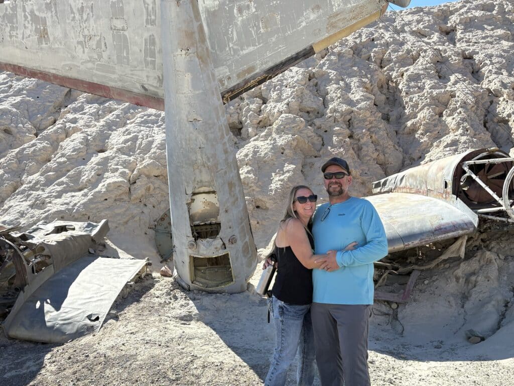 Happy couple by a vintage airplane wreck in Nevada desert, perfect for Las Vegas ATV tours or Colorado River sightseeing.