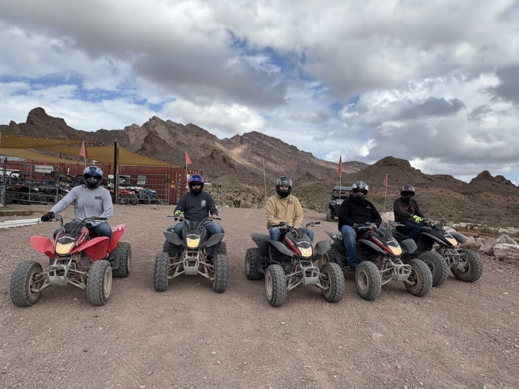 Group on ATVs in Nevada near rocky mountains, ready for an ATV tour adventure from Las Vegas; extra vehicles to the left.