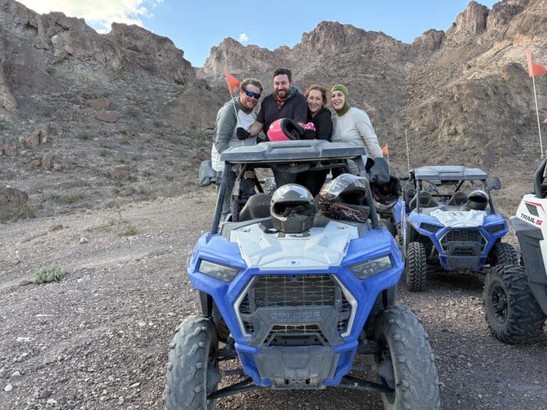 Group poses with a blue ATV on a rocky Nevada trail near Las Vegas, with ATVs and rugged hills—perfect for an ATV tour adventure.
