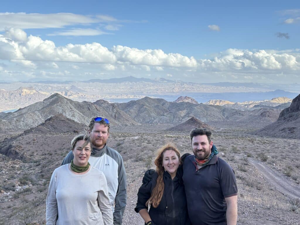 Smiling group in outdoor gear at Nevada desert near Las Vegas, mountains behind, ready for ATV tours or Colorado River sightseeing.