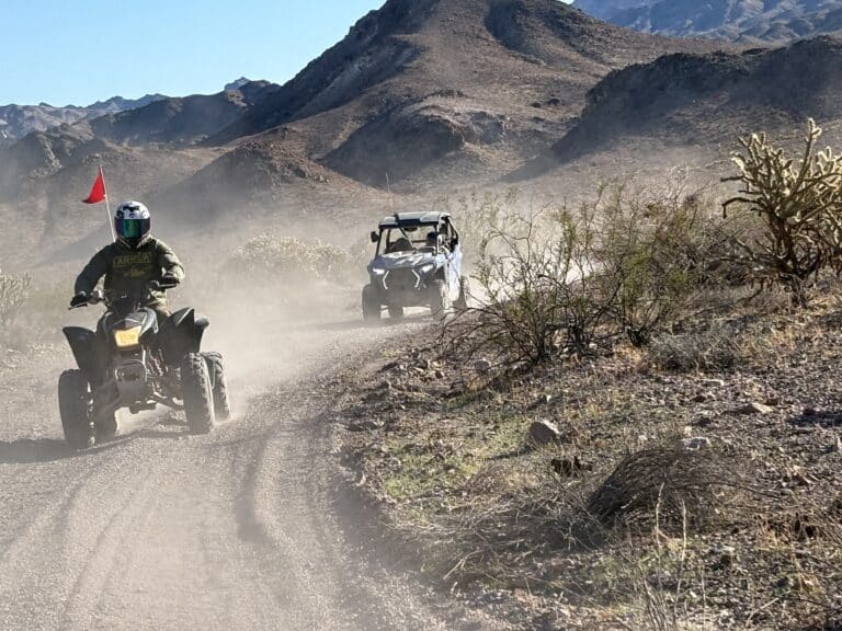 ATV tour and RZR off-road ride near Las Vegas on a dusty Nevada trail, with desert mountains and shrubs under a blue sky.