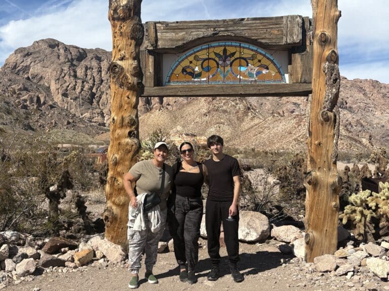 Smiling trio under rustic arch with stained glass, desert, and rocky Nevada mountains near Las Vegas Ghost Town sights.