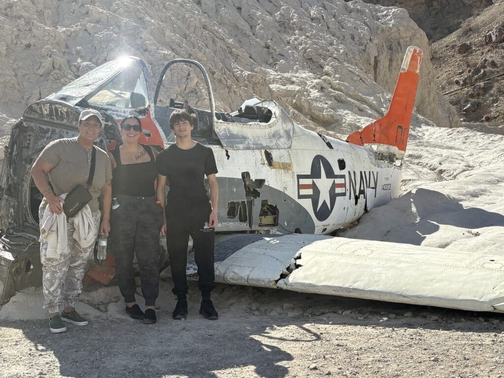 Three friends pose by a weathered US Navy plane wreck in Nevada desert near Las Vegas, perfect for ATV tours or Ghost Town adventures.