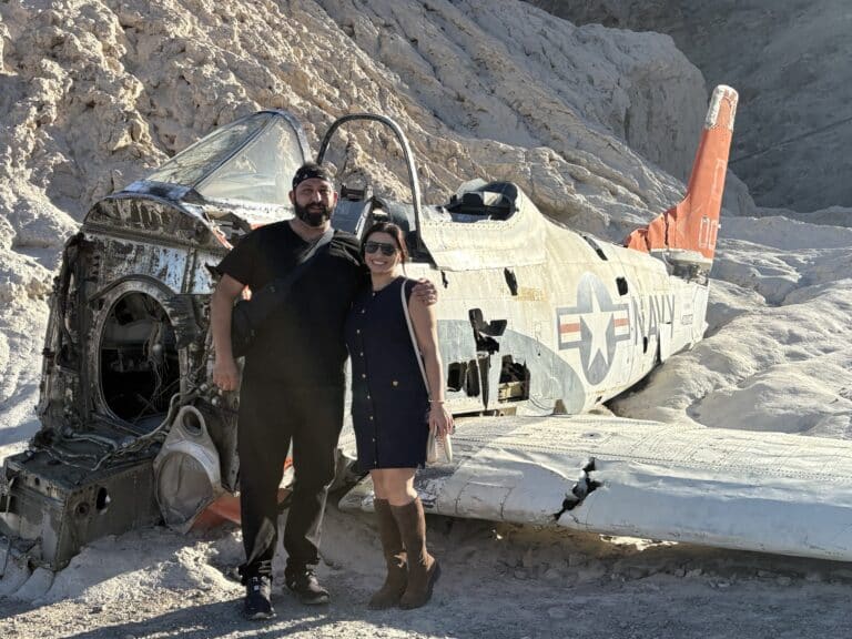 Smiling couple by abandoned U.S. Navy plane in Nevada desert near Las Vegas, perfect for RZR off-road or Ghost Town tours.