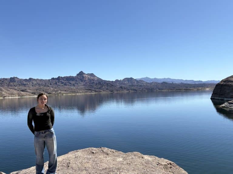 Woman in black top and jeans on rocky Nevada lakeshore near Colorado River, mountains in view, perfect for Las Vegas ATV tours.