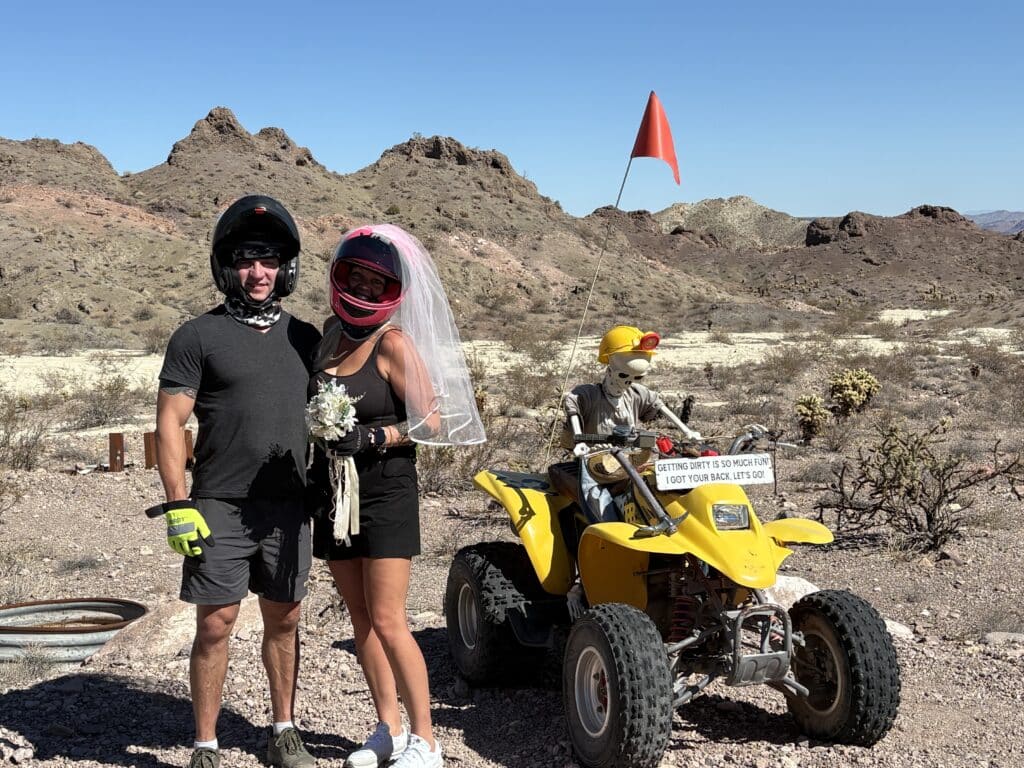 Couple in helmets, bride with veil and flowers, pose by ATV and skeleton bride near Las Vegas desert hills—perfect for Nevada ATV tours.