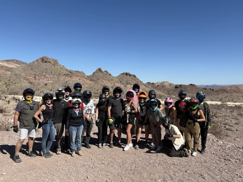 Group of people in helmets pose on rocky Nevada desert with mountains, during Las Vegas ATV tour near Colorado River under blue sky.