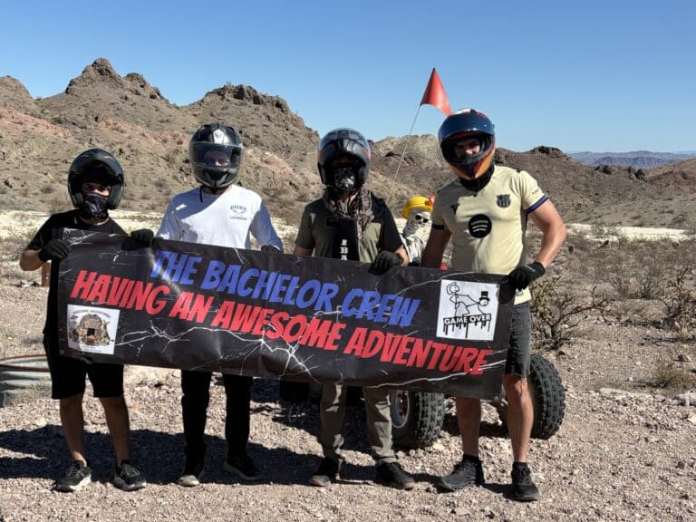 Four adventurers pose with a banner during an epic Las Vegas ATV tour near the Nevada desert and Colorado River mountains.
