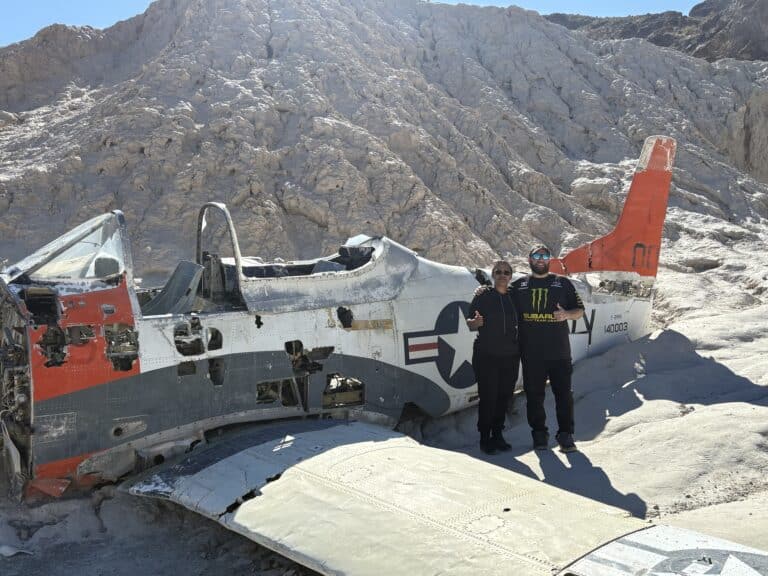Smiling duo gives thumbs up by an abandoned military plane wreck in Nevada desert near Las Vegas Ghost Town ATV tour spot.