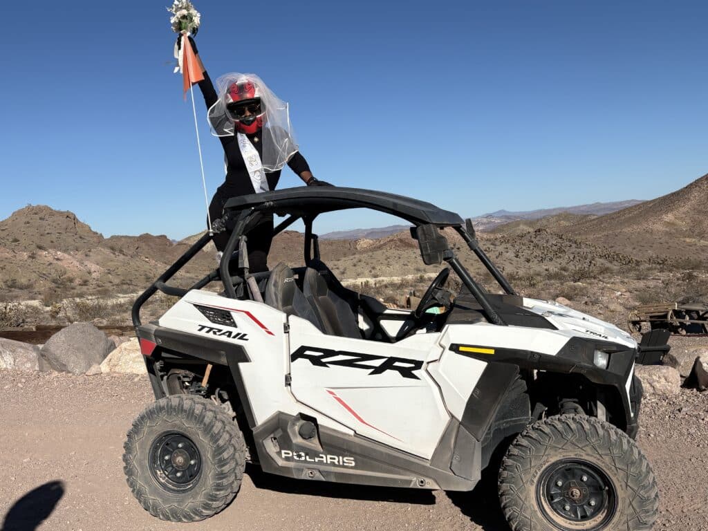 A person in veil and helmet in a white Polaris RZR holds flowers aloft during a Nevada desert ATV tour near Las Vegas.