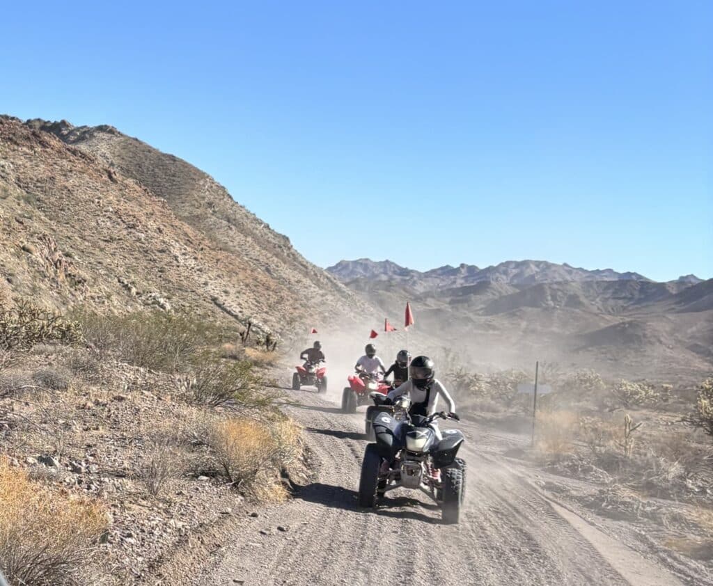 Adventurers enjoy an ATV tour on a dusty Nevada desert trail near Las Vegas with rocky hills and sparse vegetation.