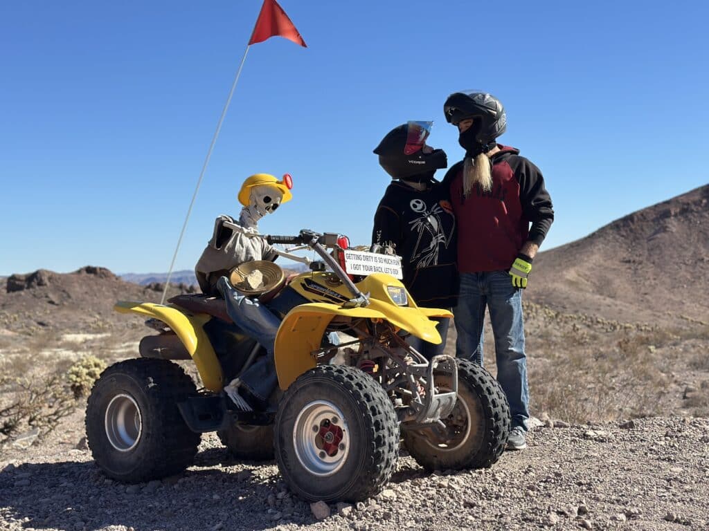 Adventurers in helmets by a yellow ATV and skeleton at a Nevada desert, perfect for Las Vegas ATV tours near the Colorado River.