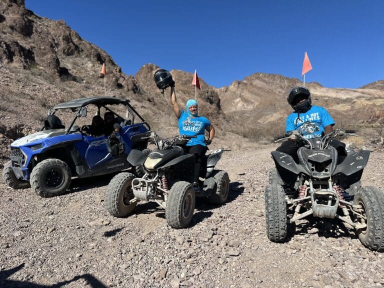 Adventurers on ATVs and a blue RZR ride Nevada’s rocky terrain near Las Vegas, with safety flags and desert mountains in view.