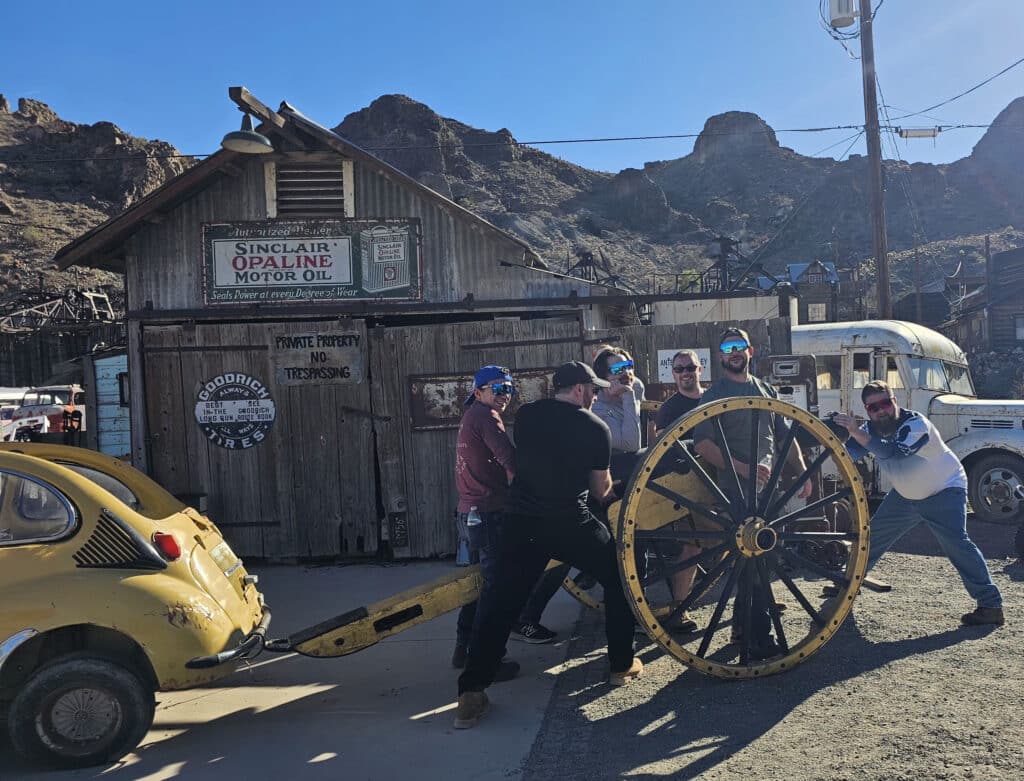 Five men in Nevada’s Ghost Town pose by a vintage yellow car and wagon wheel, perfect for ATV tours near Las Vegas.