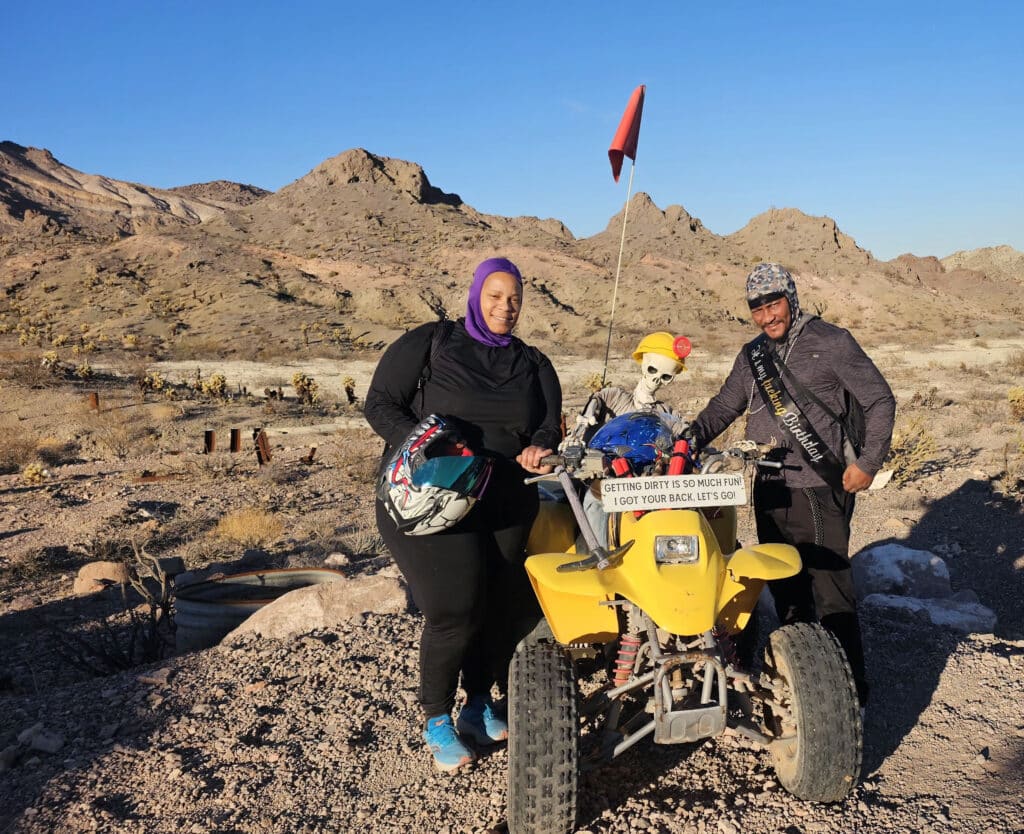 Smiling friends by a yellow ATV and skeleton in Nevada desert near Las Vegas, perfect for thrilling ATV tours or Ghost Town sightseeing.
