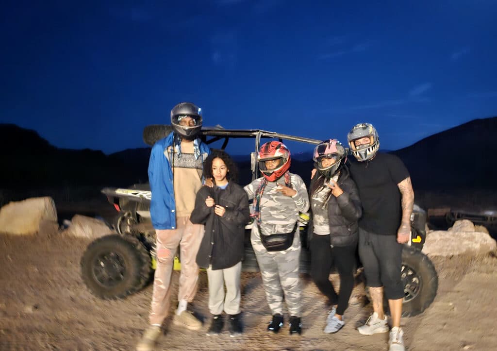 Group posing at dusk by off-road vehicle in Nevada, ready for an ATV tour near the Colorado River and Las Vegas mountains.