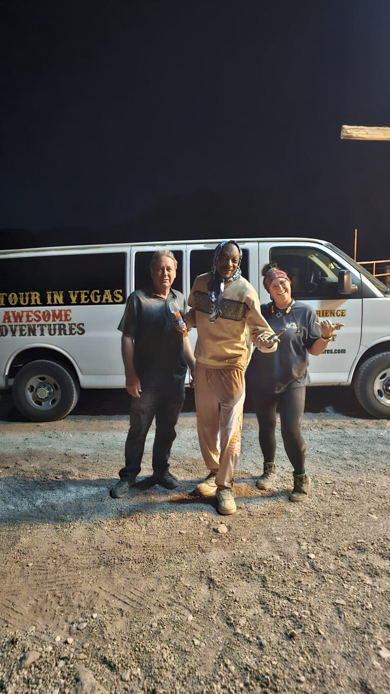 Three people smile in front of a Las Vegas tour van at night, ready for Nevada ATV tours or Ghost Town sightseeing adventures.