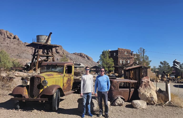 Two people in a Nevada desert ghost town near Las Vegas, standing by vintage trucks—perfect for ATV tours and sightseeing.