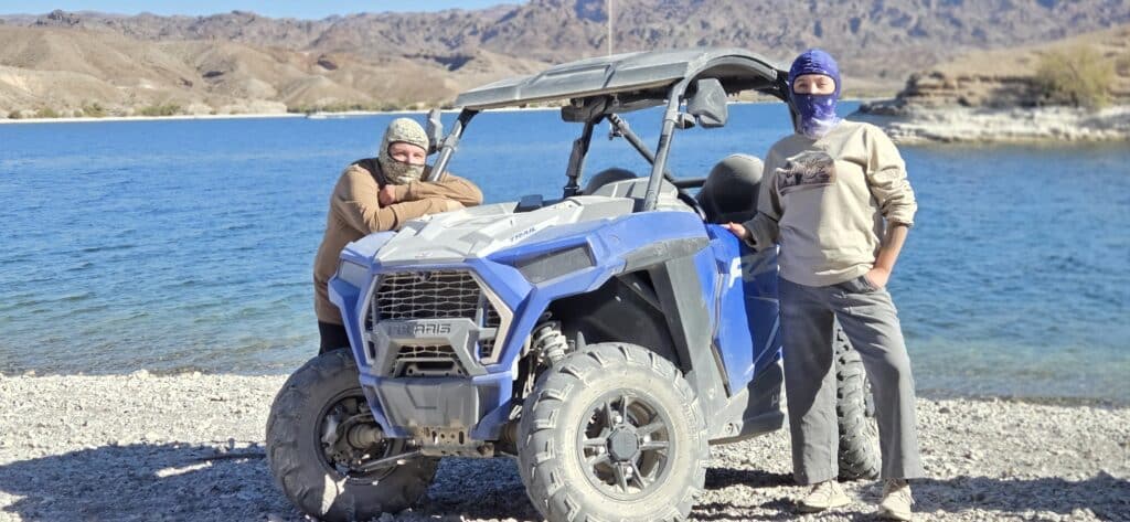 Two adventurers in sunglasses by a blue RZR at the Colorado River, Nevada, on an ATV tour near Las Vegas.