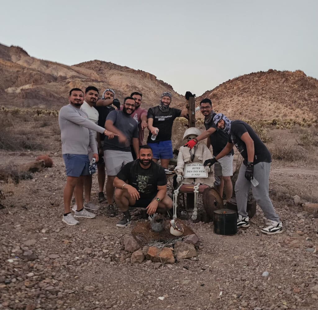 Smiling group poses by a mannequin with a sign in Nevada desert near rocky hills, perfect for Las Vegas ATV or RZR off-road fun.
