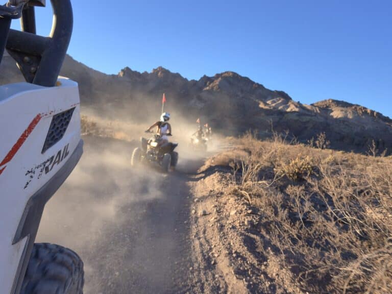 ATV riders explore a dusty Nevada desert trail near Las Vegas, mountains behind and blue sky above—perfect for off-road tours.