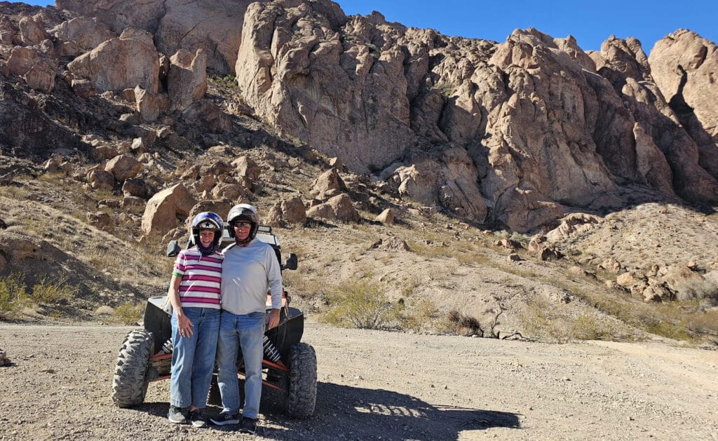 Two people in helmets stand by an off-road ATV in Nevada’s rocky desert near Las Vegas, ready for an RZR tour adventure.