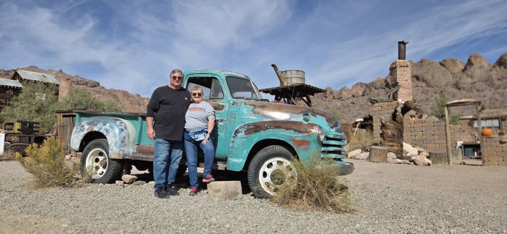 Smiling couple by a turquoise vintage truck in a Nevada desert ghost town near Las Vegas, perfect for ATV or RZR tours.