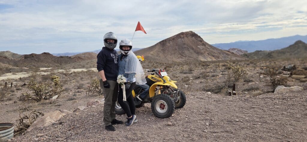 Adventurers in helmets pose by a yellow ATV with a red flag on a Nevada desert tour near Las Vegas and the Colorado River.
