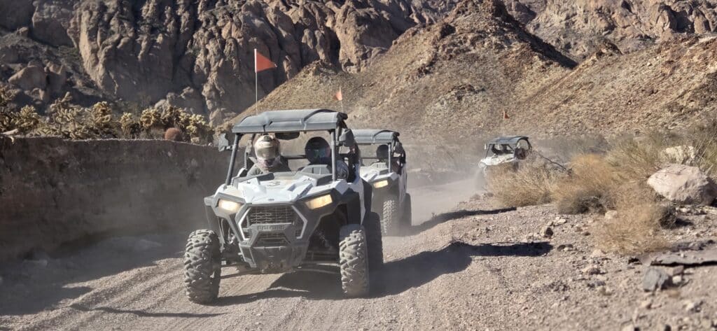 ATVs drive on a dusty desert trail near Las Vegas, Nevada, with helmeted riders and mountains—perfect for ATV tours or RZR adventures.