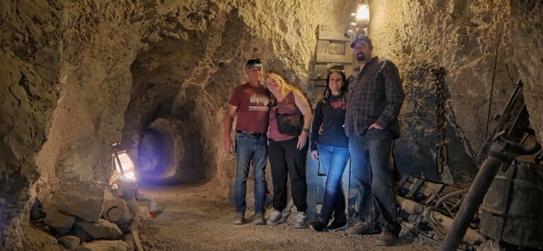 Four adults explore a dim Nevada mine tunnel near Las Vegas, surrounded by tools—perfect for Ghost Town sightseeing tours.