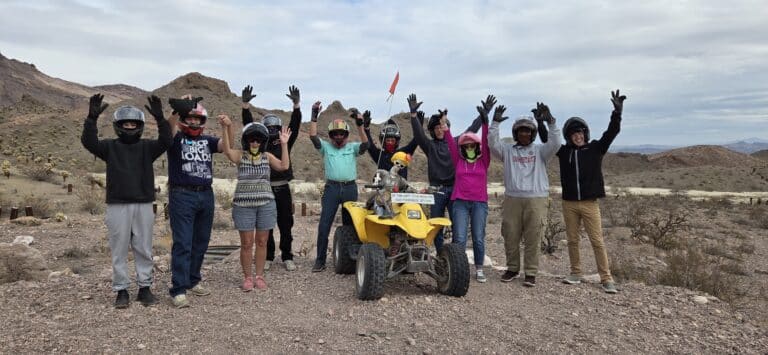 Group enjoying an ATV tour near Las Vegas, Nevada, posing with helmets on rocky desert terrain and mountains in the background.