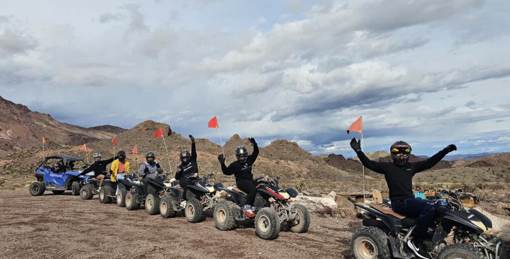 Group in helmets enjoys a Las Vegas ATV tour on a desert trail; RZR off-road ride and Nevada scenery in the background.