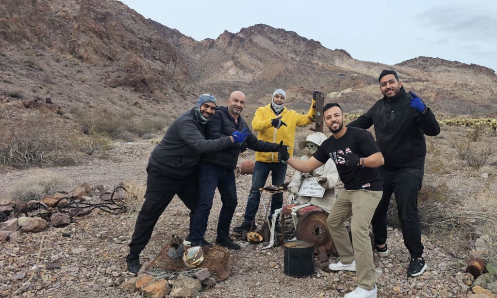 Five men in Nevada desert near Las Vegas, smiling and posing with a skeleton chair on a Ghost Town sightseeing adventure.