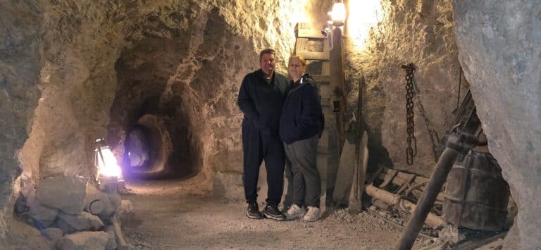Two people in casual wear explore a dim, rocky Nevada tunnel near Las Vegas with mining tools—perfect for ATV tours or Ghost Town visits.