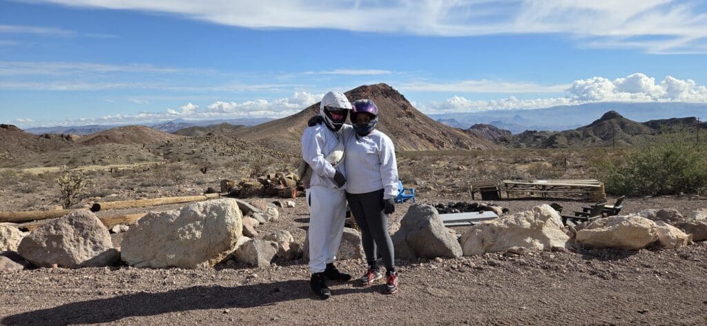 Two people in white hoodies and helmets on a Nevada desert ATV tour near Las Vegas with rocky terrain and mountains in view.