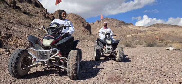 Two people in white ride ATVs with red flags on a rocky Nevada desert trail near mountains—Las Vegas ATV tour adventure.