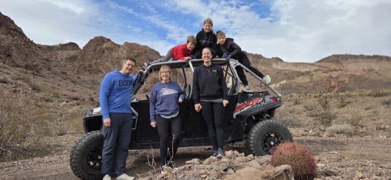 Family smiles by a black RZR in Nevada’s rocky desert, kids on top, perfect for Las Vegas ATV tours or Colorado River adventures.